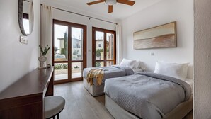Ein Schlafzimmer mit zwei Betten, einem Deckenventilator, einem großen Fenster und Blick ins Freie.