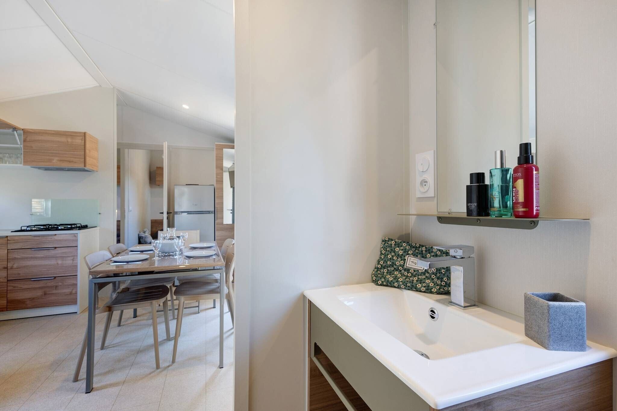 A modern kitchen with a dining area, a white sink, and a mirror above the sink.
