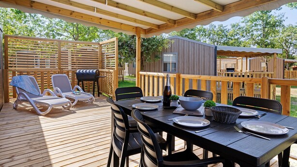 Een overdekt terras met een eettafel, lounge stoelen en een barbecue.