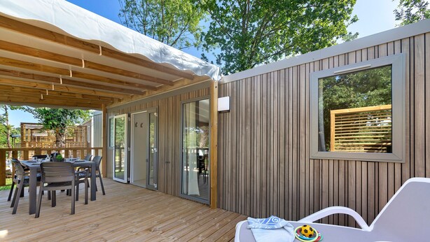 Une terrasse en bois avec une table et des chaises, un espace couvert et une fenêtre avec des stores.