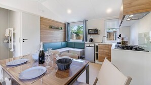 Une cuisine compacte dotée d’une cuisinière intégrée, un coin repas avec une table pour deux personnes et un espace détente avec un banc.
