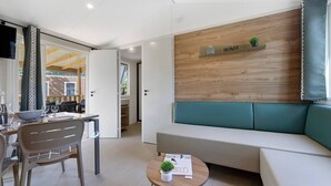 A modern living room with a sofa, a dining table with chairs, a small table with a plant, and a wall-mounted shelf with a plant and the word 'HOME'. - “Evasion 52” Mobile Home with Shared Pool and Terrace (Saint-Gervais)