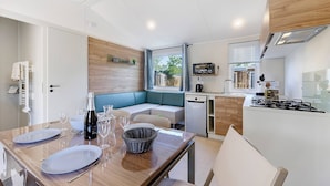 A compact kitchen with a built-in stove, a dining area with a table set for two, and a seating area with a bench. - “Evasion 52” Mobile Home with Shared Pool and Terrace (Saint-Gervais)