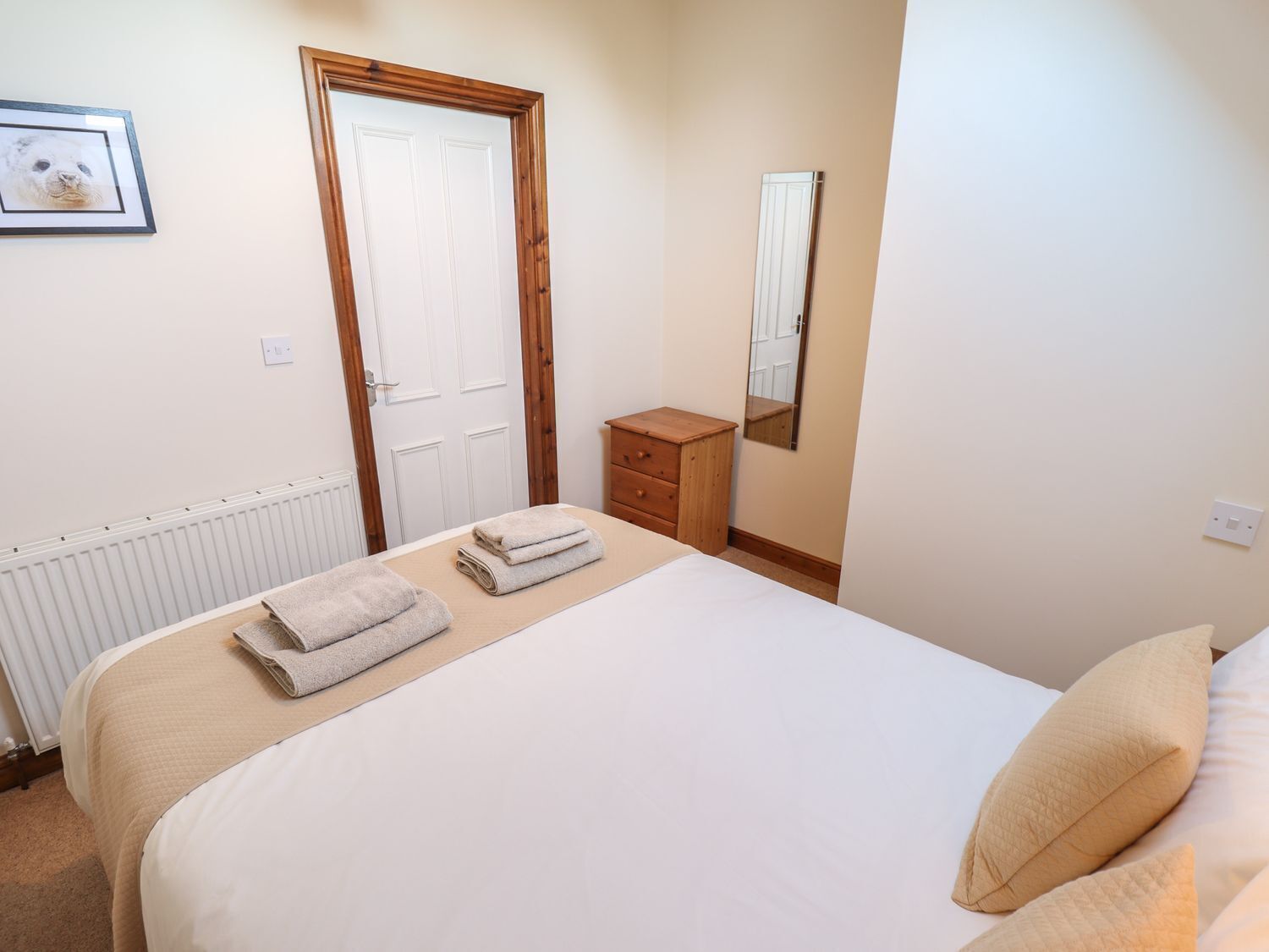 A bedroom with a bed, a wooden dresser, a mirror, and a framed picture on the wall.