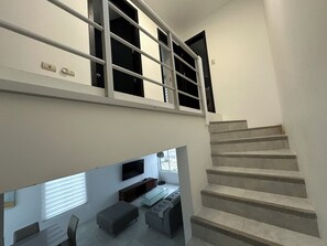 Un intérieur moderne avec un escalier menant à un niveau supérieur, un téléviseur à écran plat fixé au mur et un coin salon avec une table basse en verre.