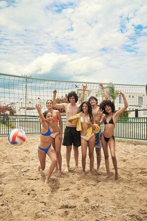 Un groupe de personnes se trouve sur une plage de sable, avec un filet de volley-ball en arrière-plan.
