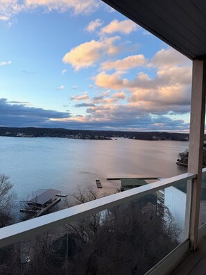 A view of a lake from a balcony with a railing, a dock, and buildings in the distance. - Modern Lakeview Getaway located on the Lake of the Ozarks (Lake Ozark)