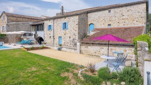 Un edificio de piedra con piscina, zona de estar al aire libre y un patio cubierto.