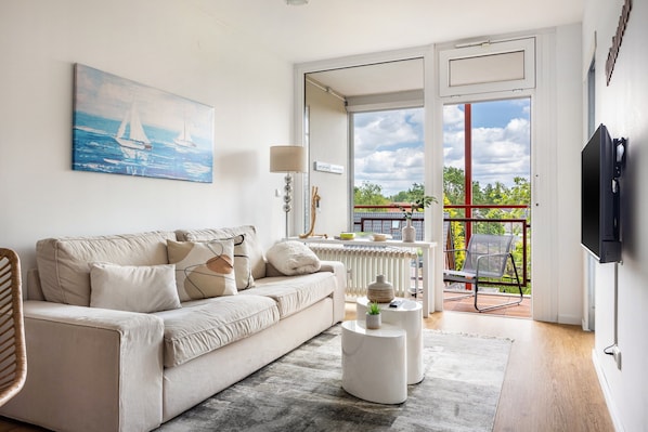 A living room with a sofa, coffee table, and a painting of sailboats. - Luxurious Small Coastal Nest Apartment Directly on Lake Steinhude (Wunstorf)