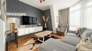 A modern living room with a black and white patterned wall, a flat-screen TV, a wooden coffee table, a grey armchair, and a sofa with patterned cushions. - Apartamenty Sun & Snow Villa Mistral (Świnoujście)