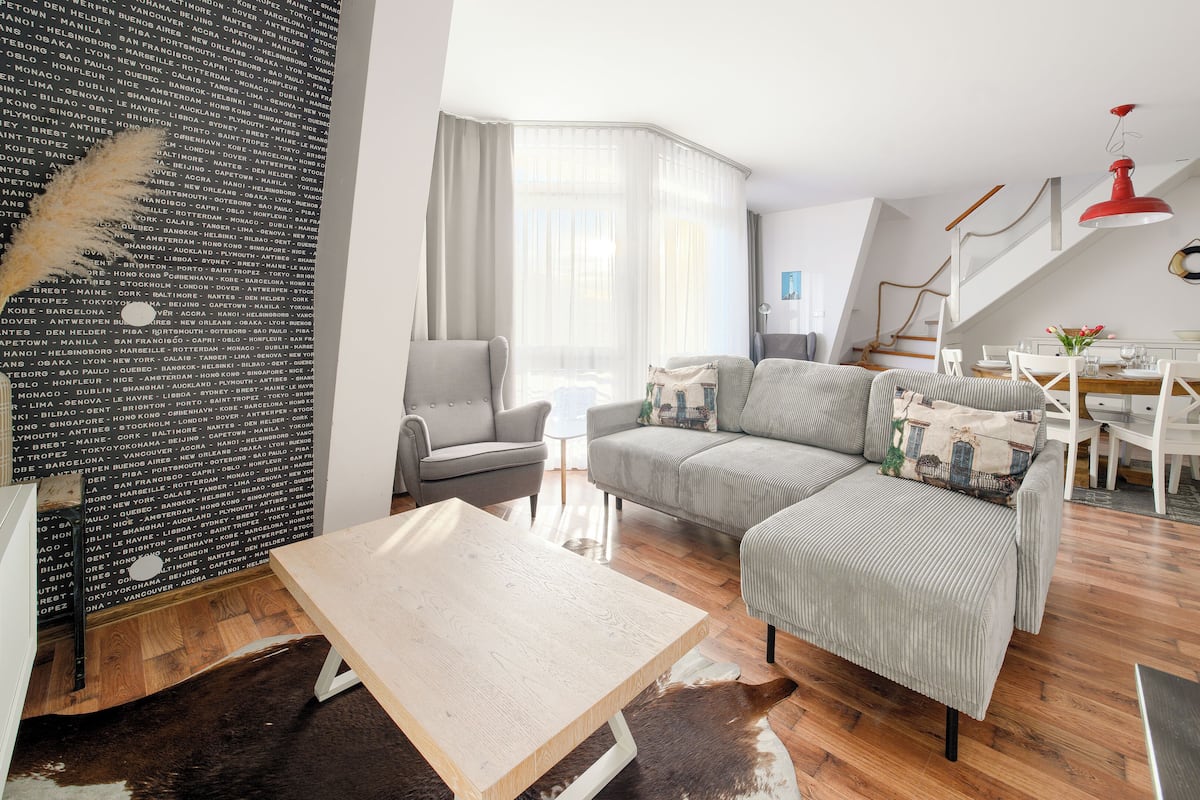 Ein modernes Wohnzimmer mit einem grauen Sofa, einem Holztisch und einem Essbereich mit einem weißen Tisch und Stühlen.