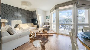 A modern living room with a leather sofa, a coffee table, and a leather rug. There is a large window with a view of the city. - Apartamenty Sun & Snow Villa Mistral (Świnoujście)