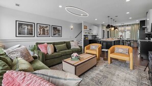 Un salon moderne avec un canapé, des fauteuils et une table basse. Un escalier mène à un niveau supérieur.