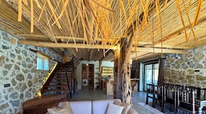 A rustic interior with a stone wall, wooden staircase, and a dining area with chairs.