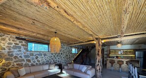 Un ambiente rustico con pareti in pietra, soffitto in legno, un divano, un lampadario e un angolo cottura.