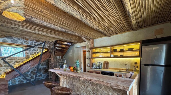 A rustic kitchen with a wooden bar, stone walls, and a built-in refrigerator.