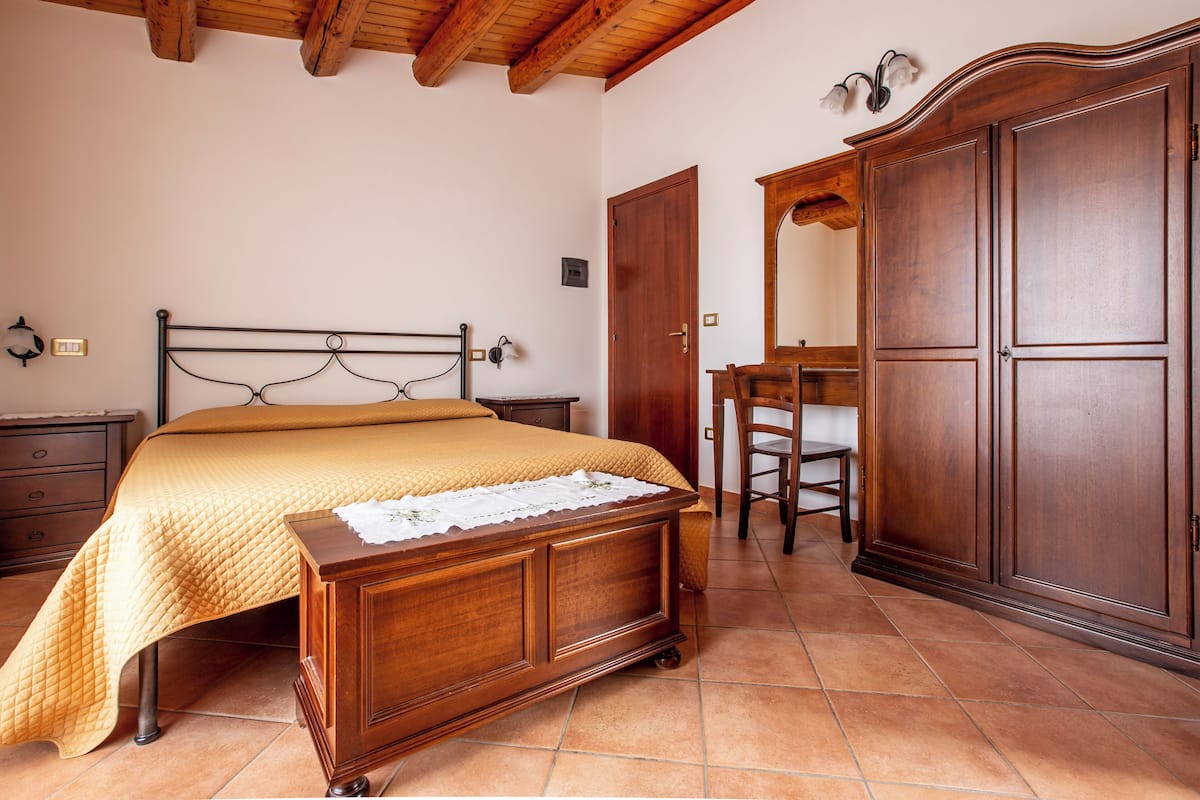 A bedroom with a bed, wooden wardrobe, a chair, and a desk.