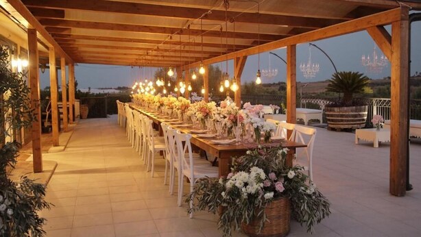 Un área de comedor al aire libre con mesas y sillas de madera, decorada con flores y luces de cadena.
