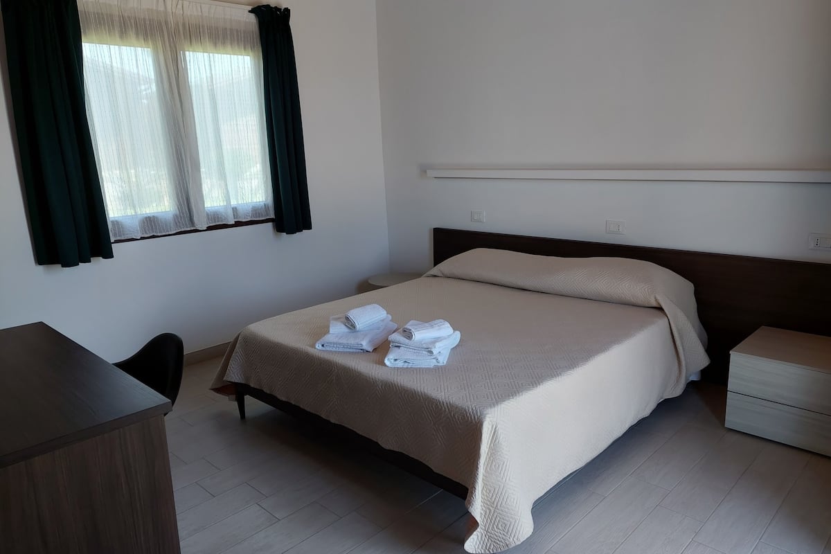 A hotel room with a bed, a desk, and a window with curtains.