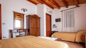 Un dormitorio con una cama, un armario de madera, un escritorio con silla, un televisor y una ventana con cortinas.