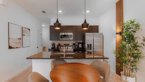 A modern kitchen with a central island, stainless steel appliances, pendant lighting, and a dining area with a round table and chairs. - 3BR apartment with heated pool near Disney (Kissimmee)