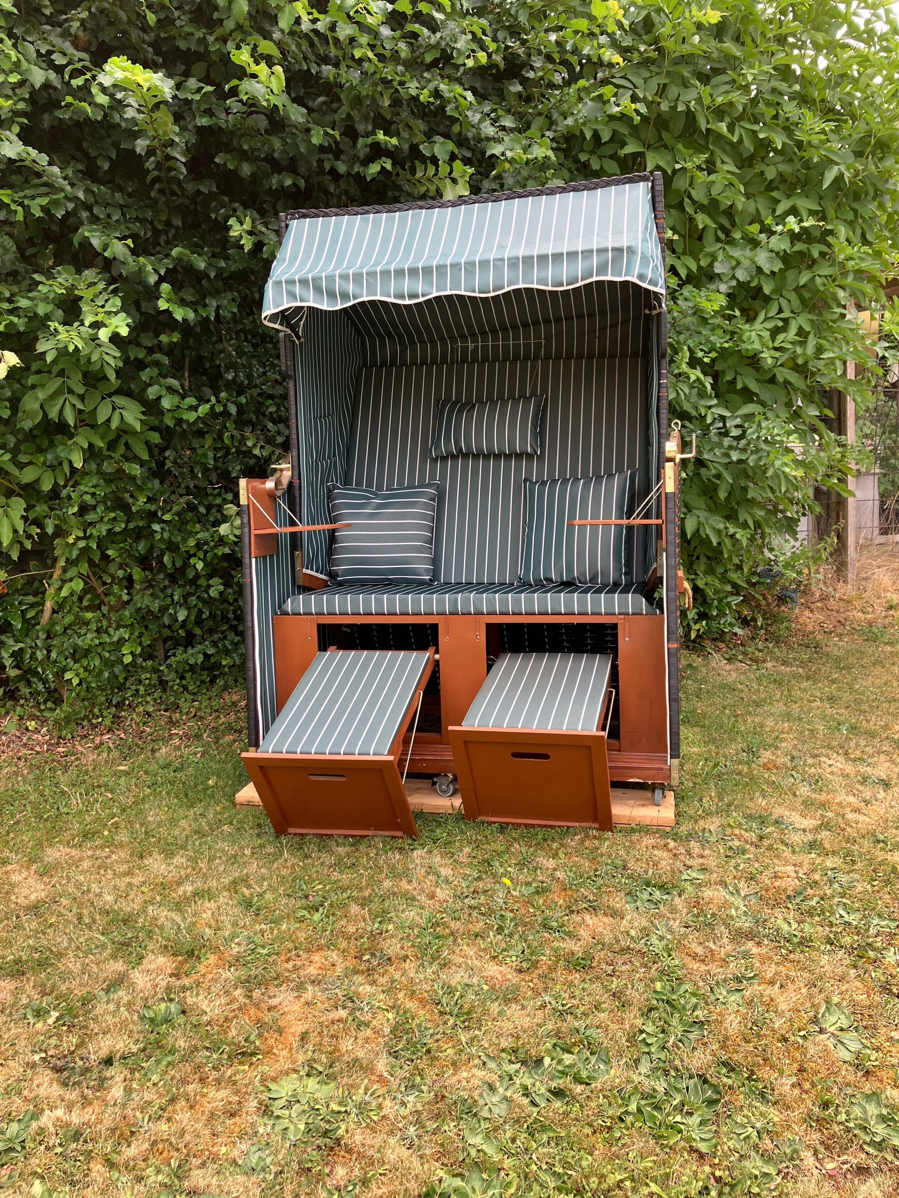 Ein Sitzbereich im Freien mit Streifenmuster und einem Sonnensegel, umgeben von viel Grün.