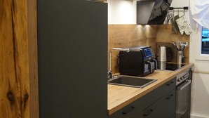 Une cuisine moderne avec des meubles de couleur sombre, un plan de travail en bois, une machine à café et une fenêtre avec des rideaux.