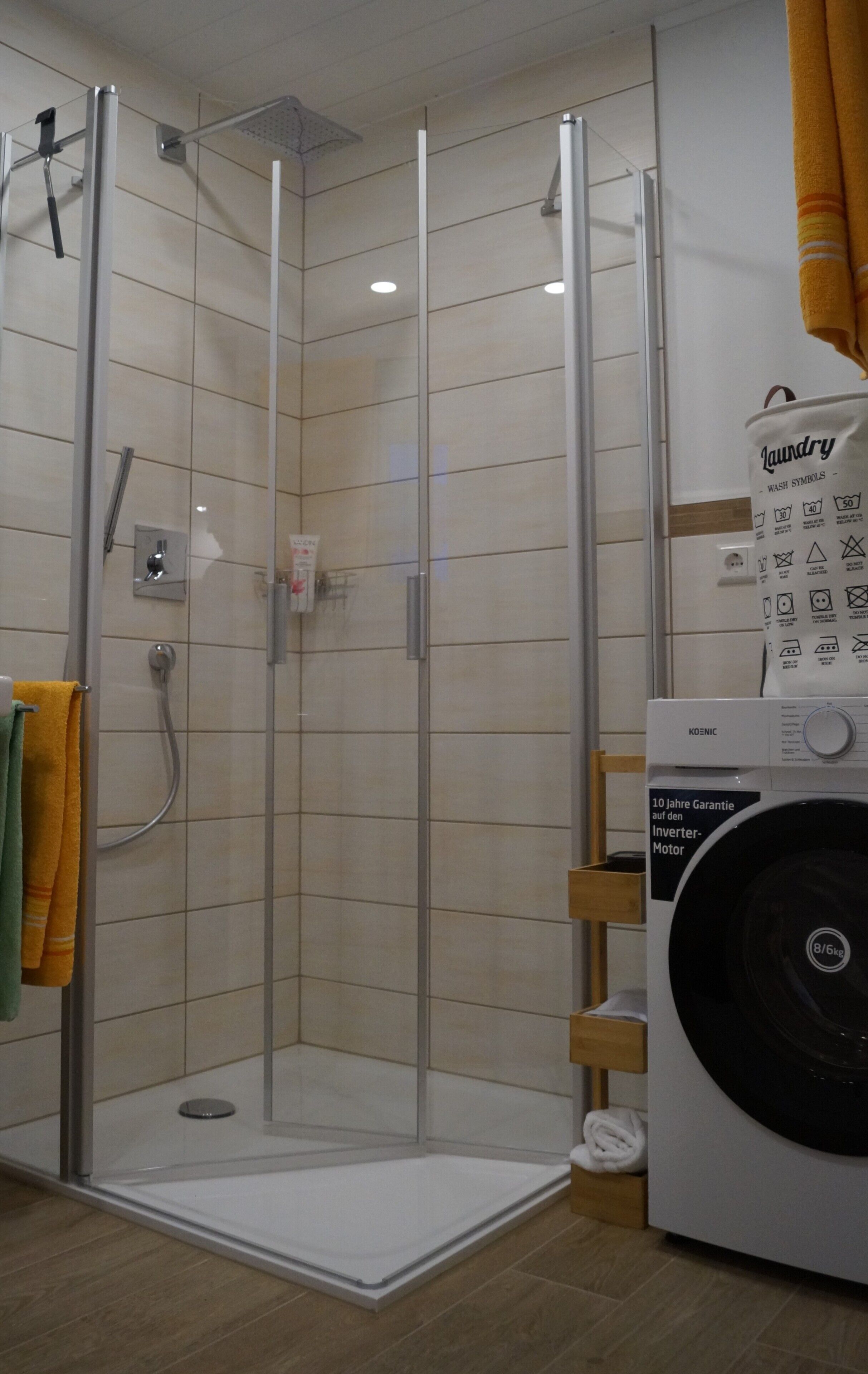 A shower with a glass door, a washing machine, and a laundry symbol bag.