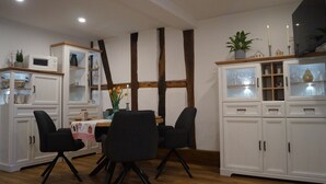 Un espace repas comprenant une table, des chaises, des meubles blancs et une poutre en bois au plafond.