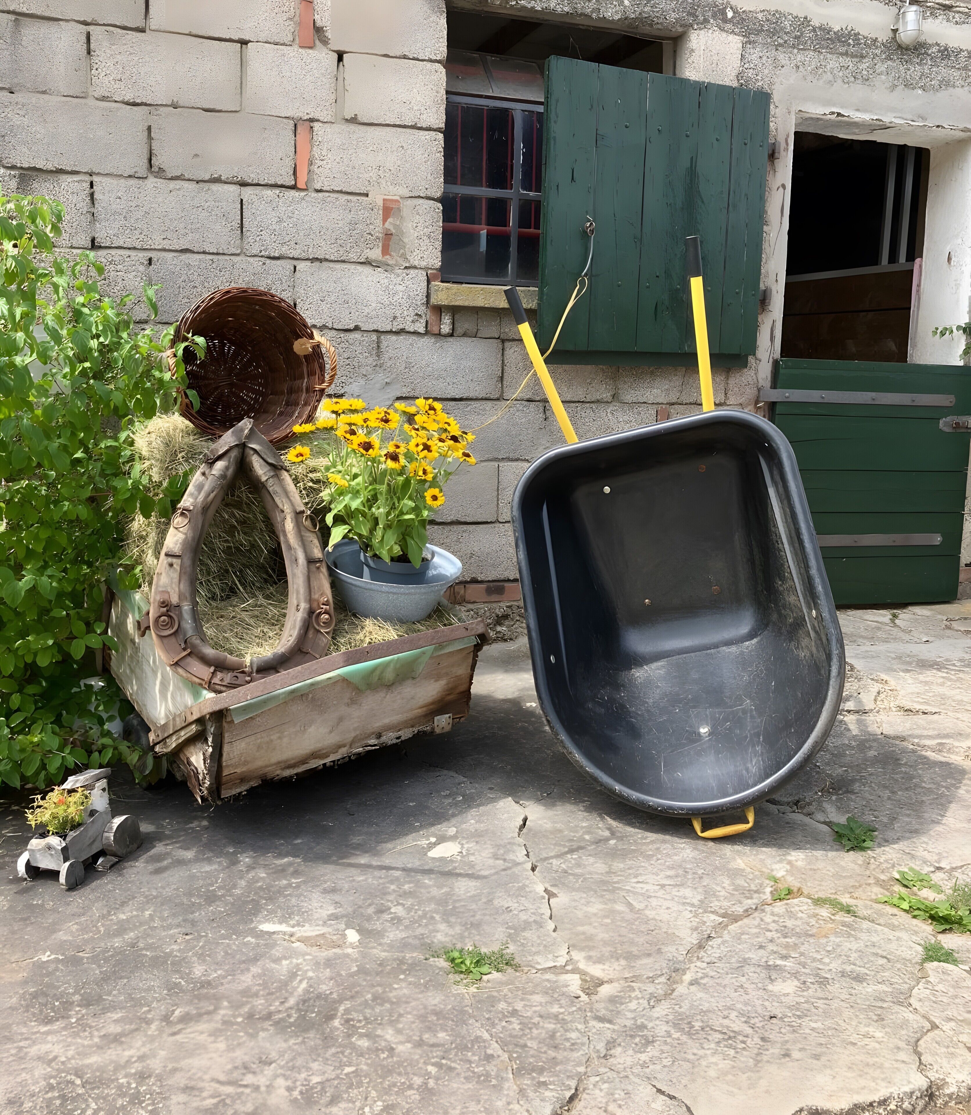 Une brouette, un chariot en bois rempli de foin et de fleurs, et une porte verte.