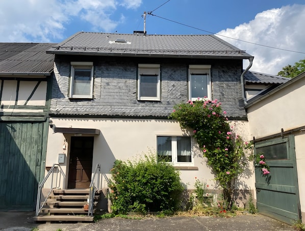 Une maison à deux étages, avec un toit gris, une porte d’entrée et un escalier menant à l’entrée.