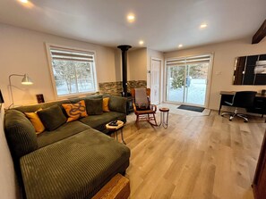 A living room with a green sofa, a fireplace, and a large window. - Chalet Le Bray (Rawdon)