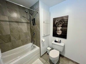 A modern bathroom with a bathtub, shower, toilet, and a wooden artwork on the wall. - Chalet Le Bray (Rawdon)