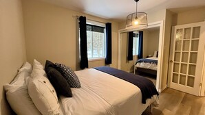 Un dormitorio con cama, ventana con cortinas, puerta con paneles de vidrio y lámpara en el techo.