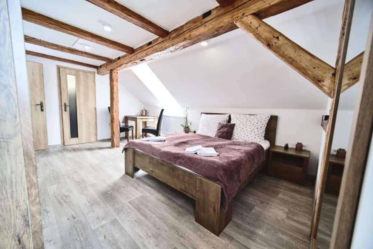 A bedroom with a wooden ceiling, a bed with a red blanket, a nightstand, and a desk with a chair.