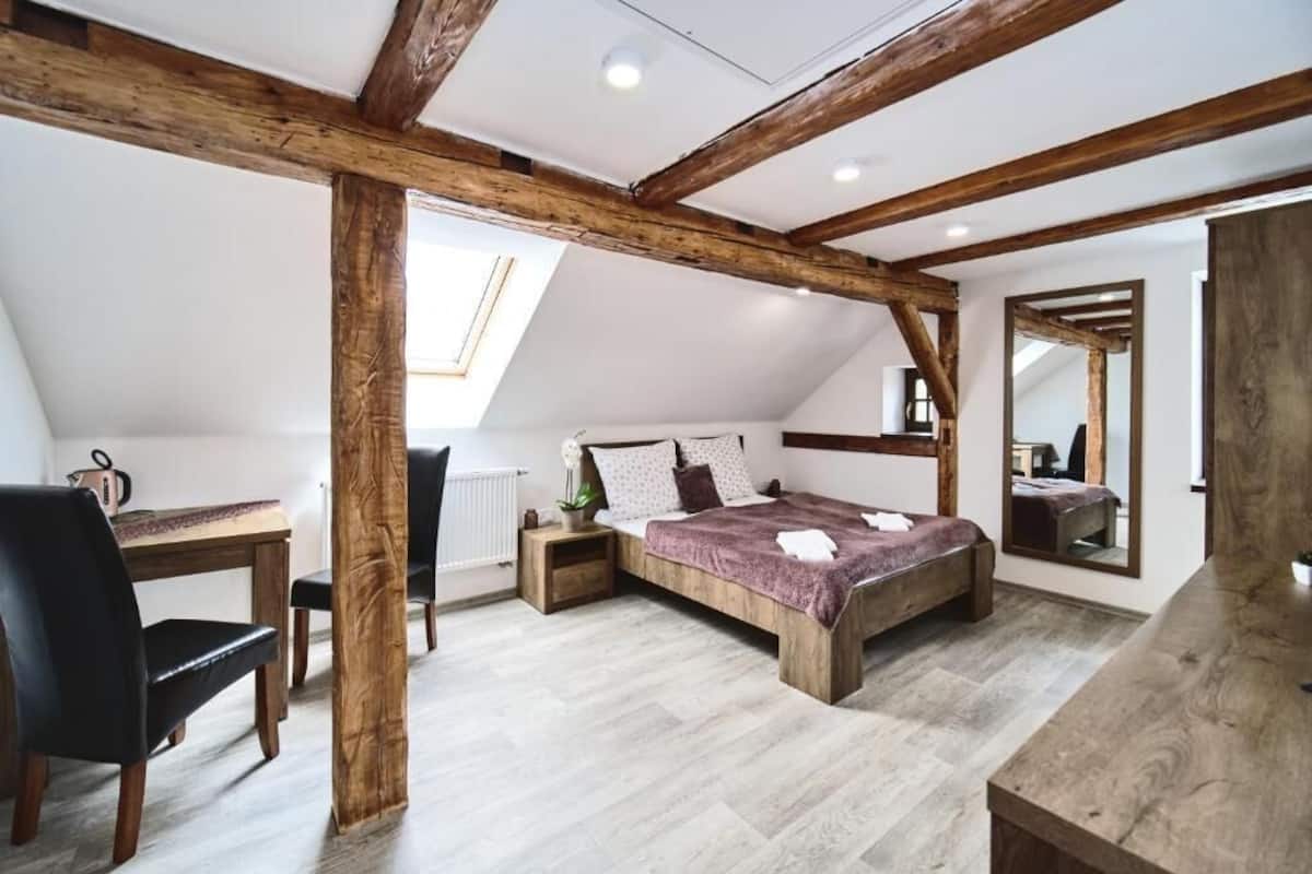 A bedroom with a sloped ceiling, wooden beams, a bed, a desk, and a chair.