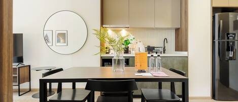 A modern kitchen with wooden cabinets, a built-in oven, and a refrigerator. There is a dining table with chairs and a vase with flowers.