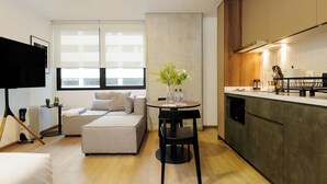 Una sala de estar moderna con un sofá, una mesa de comedor con sillas, un televisor y una zona de cocina con mostrador y armarios.