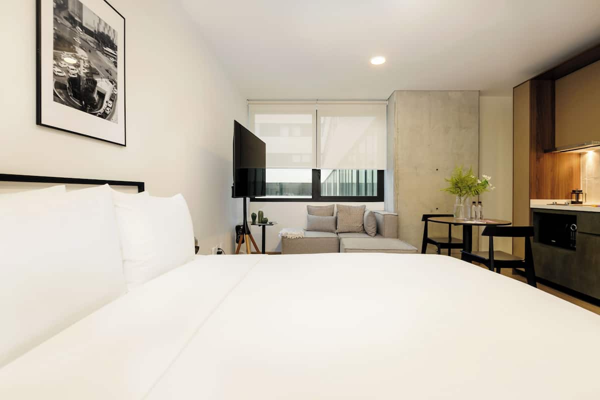 Een moderne hotelkamer met een groot bed, een bank, een kleintje tafeltje, een televisie en een kitchenette.