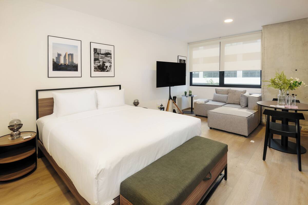 Een moderne hotelkamer met een groot bed, een bank, een kleintje tafeltje met een vaas en een televisie.