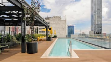 Una piscina en la azotea con cubierta de madera, sillas de descanso y plantas en macetas.