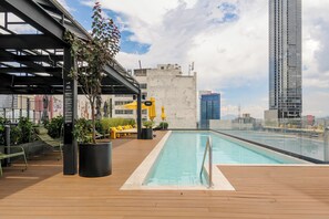 Piscina no terraço com deck de madeira, espreguiçadeiras e plantas em vasos.