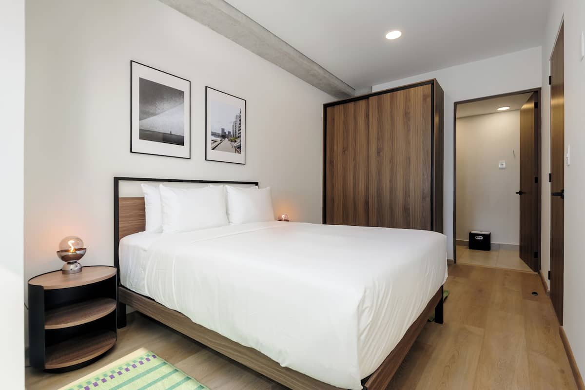 Een moderne slaapkamer met een groot bed, een nachtkastje met een lamp en twee ingelijste foto's aan de muur.
