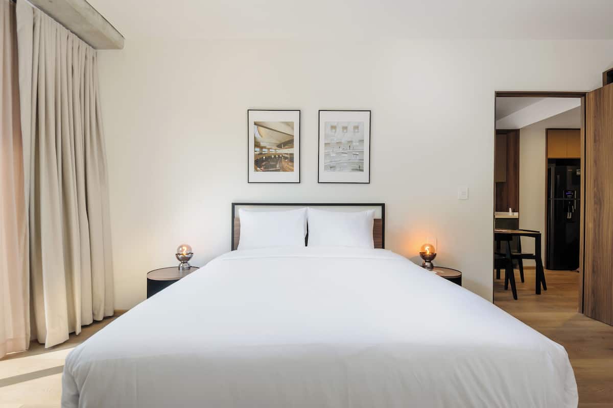 Een hotelkamer met een groot bed, twee nachtkastjes met lampen, een houten garderobe en een deur naar een badkamer.