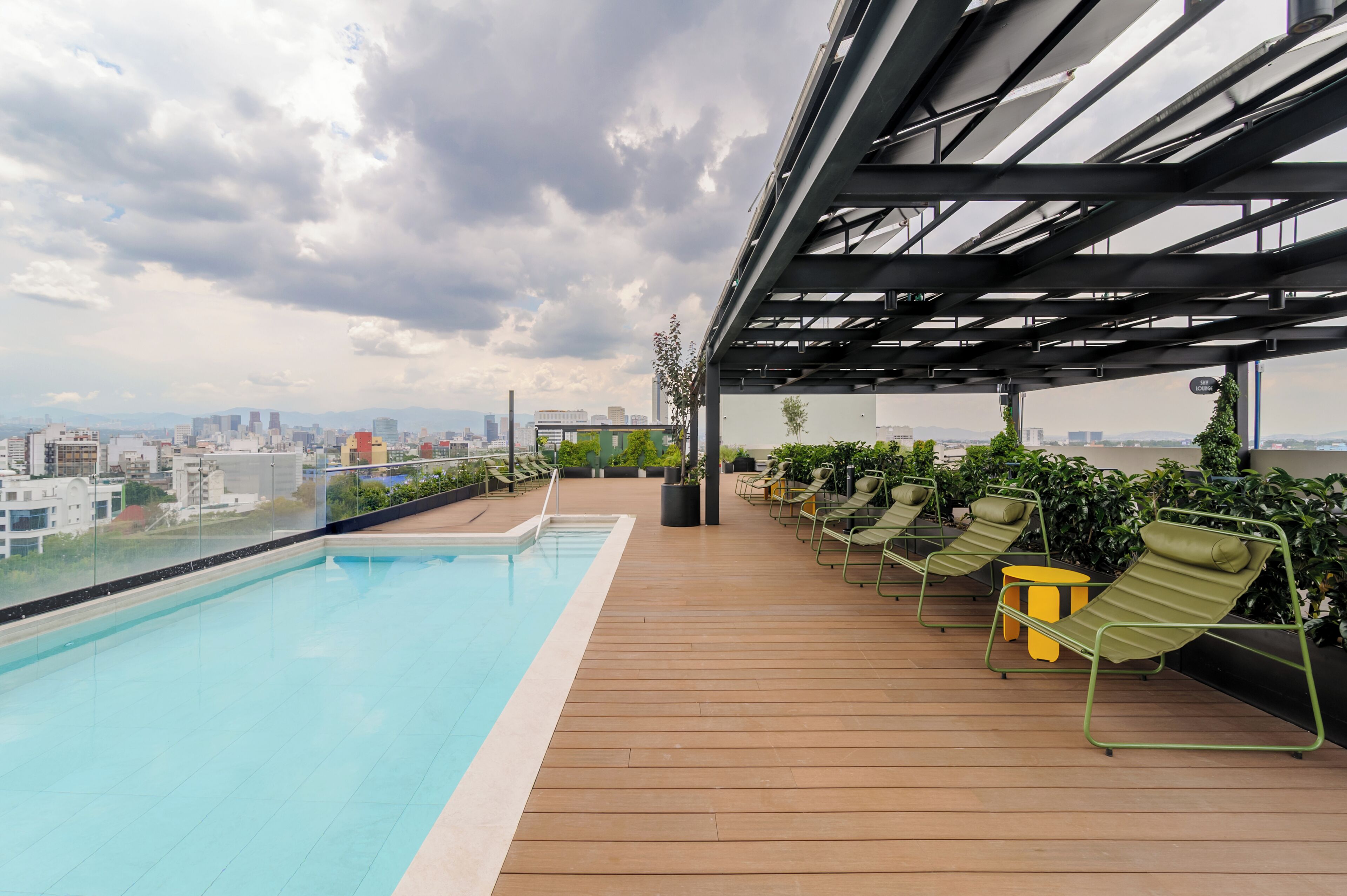 Una piscina en la azotea con vista a la ciudad, sillas de descanso y una pérgola.