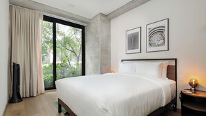 Una habitación de hotel moderna con una cama grande, vistas a zonas verdes a través de un ventanal corredera y dos cuadros en la pared.