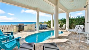 Un espace extérieur abrité comprenant une piscine, des chaises longues, un barbecue et une vue sur l’océan.
