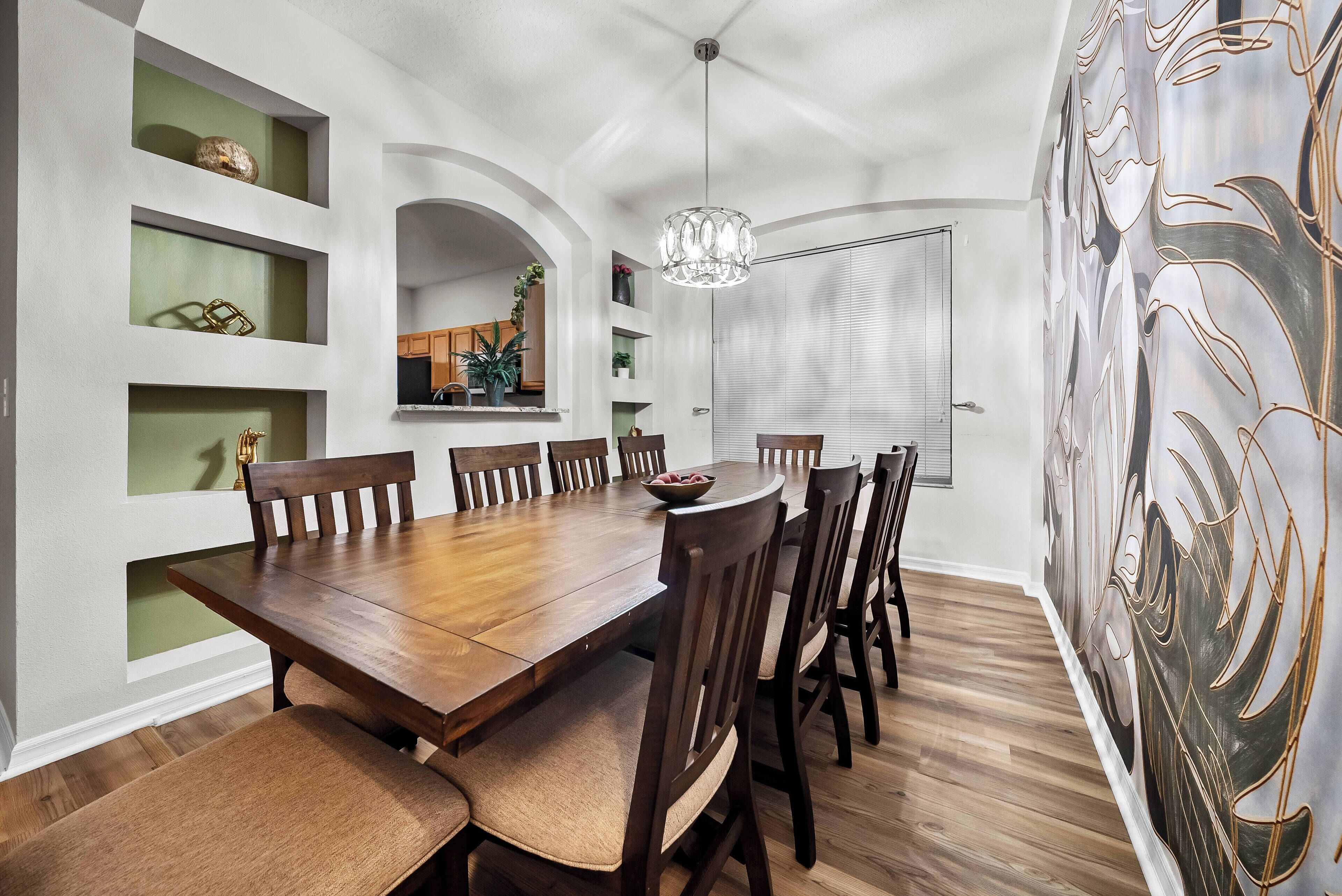 A dining area with a wooden table and chairs, a chandelier, and shelves with decorative items.