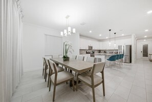 A modern kitchen with white cabinets, a central island, and a dining area with a wooden table and chairs. - 6BR house sleeps 14 with game room in davenport (Davenport)