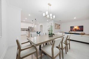 Ein moderner Essbereich mit Holztisch und -stühlen, einer Chandelierleuchtre und einer Küche im Hintergrund.